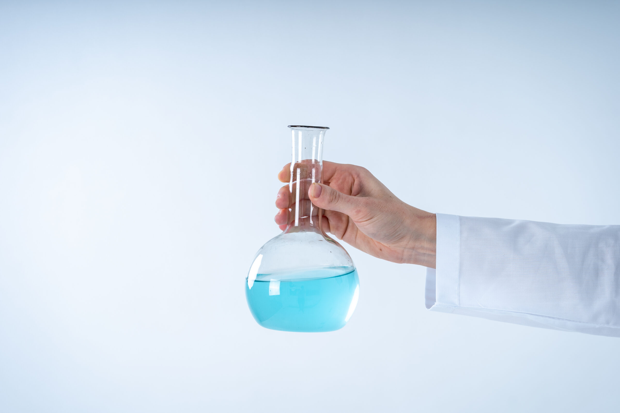 Cropped view of chemist woman in lab uniform making laboratory experiment, holding medical glass bottle with blue liquid, standing isolated on white background with copy space